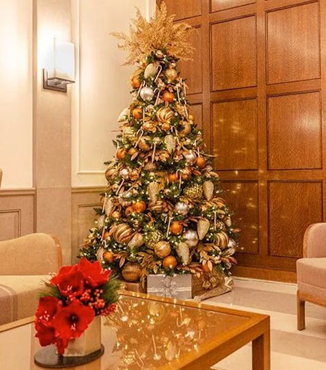 A majestically decoreated Christmas tree, stuffed with glistening ornaments and golden pine cones, stands in the seating area of a hotel lobby