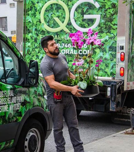 One of QG's experts emerges from a delivery van, carrying an arrangement of pink orchids