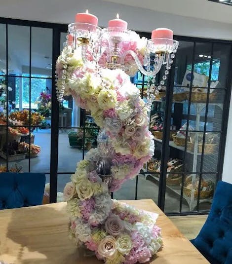 A fancy, spiraling bouquet winds and climbs around a crystal vase, presented at the counter of a flower shop