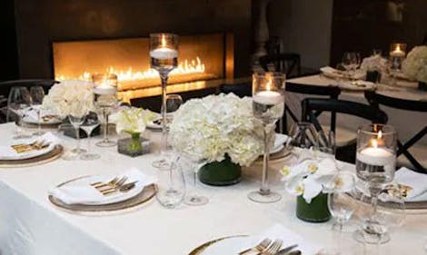 White flowers of several varieties serve as a centerpiece upon a small, elegant dinner setting