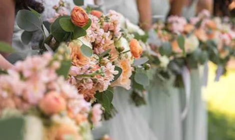 Close-up of several bridesmaids' hands as they hold matching orange, pink and white wedding bouquets